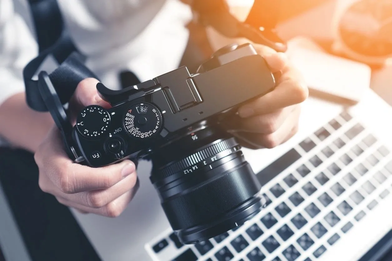 A person holding a camera in front of a laptop.